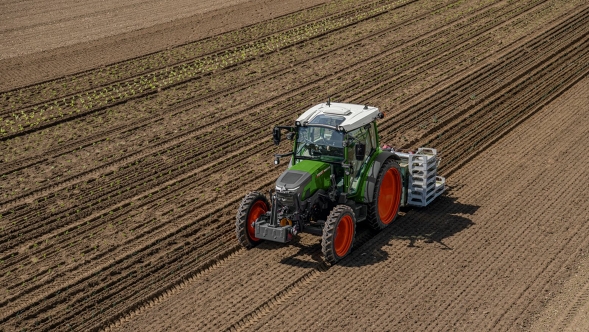 A Fendt e100 Vario driving in a field and working the soil
